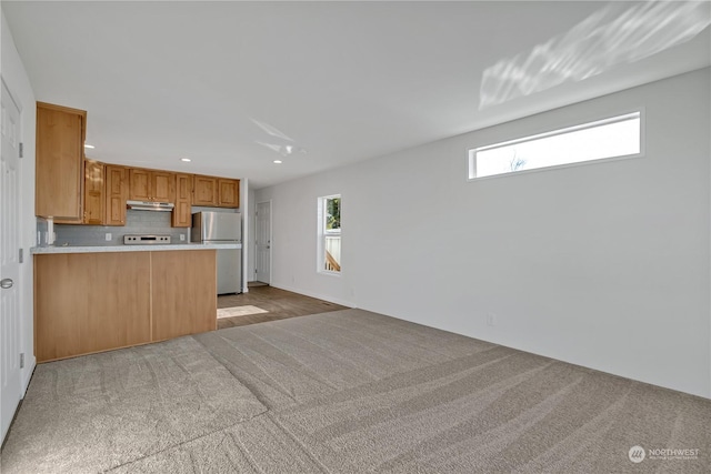 kitchen featuring stainless steel fridge, light colored carpet, kitchen peninsula, and plenty of natural light