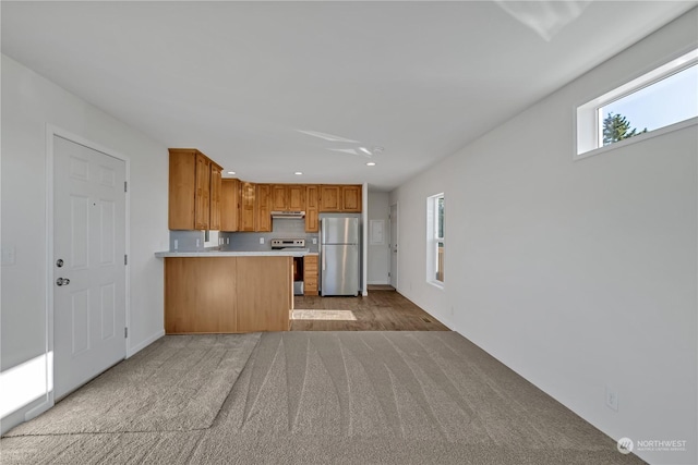 kitchen featuring light colored carpet, appliances with stainless steel finishes, kitchen peninsula, and plenty of natural light