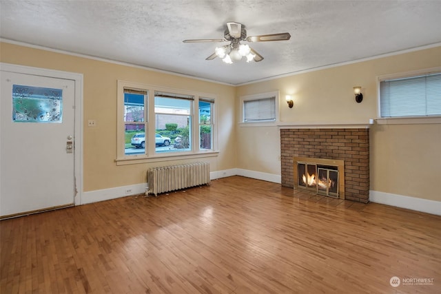 unfurnished living room featuring radiator heating unit, a fireplace, wood-type flooring, crown molding, and a textured ceiling