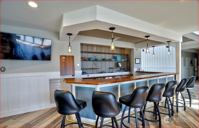 bar with butcher block counters, light hardwood / wood-style floors, and hanging light fixtures