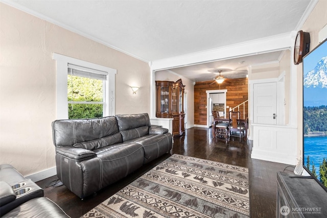 living area featuring baseboards, dark wood finished floors, ceiling fan, ornamental molding, and wood walls