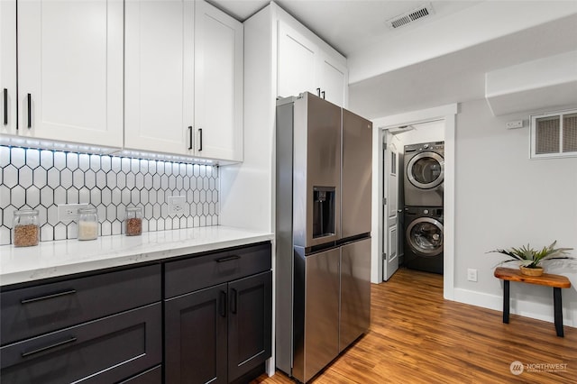 kitchen featuring stacked washing maching and dryer, white cabinets, decorative backsplash, stainless steel fridge with ice dispenser, and light wood-type flooring