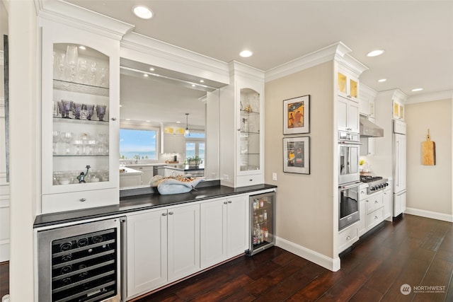 bar with crown molding, dark wood-type flooring, stainless steel appliances, white cabinets, and beverage cooler