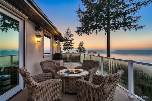 balcony at dusk with an outdoor fire pit and a water view