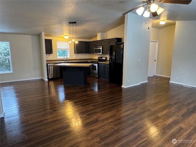 kitchen with dark wood-type flooring, vaulted ceiling, hanging light fixtures, appliances with stainless steel finishes, and a kitchen island