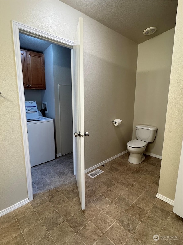 bathroom with washer / dryer, a textured ceiling, and toilet