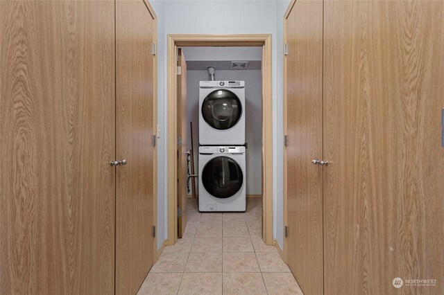 laundry area with stacked washer / drying machine and light tile patterned floors