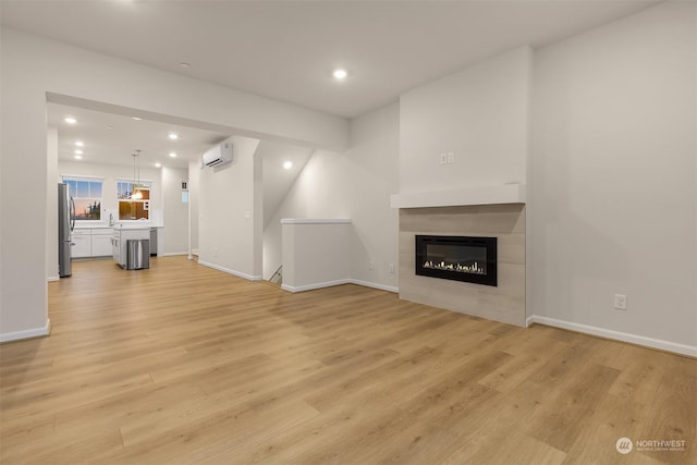 unfurnished living room featuring a wall mounted air conditioner, light hardwood / wood-style flooring, and a fireplace