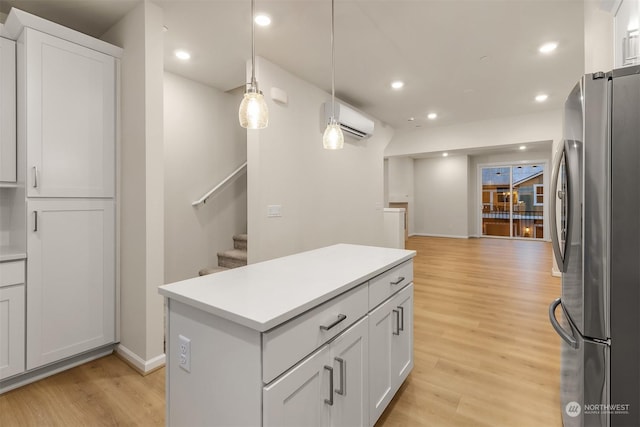 kitchen featuring pendant lighting, white cabinetry, stainless steel fridge, light hardwood / wood-style floors, and a wall unit AC