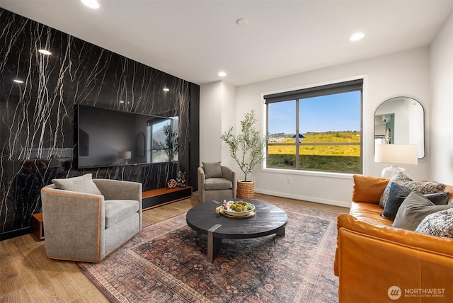 living area featuring an accent wall, baseboards, wood finished floors, and recessed lighting