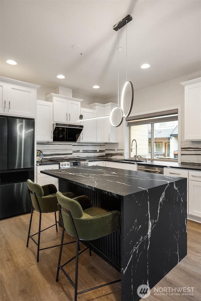 kitchen with a spacious island, backsplash, appliances with stainless steel finishes, a sink, and wood finished floors