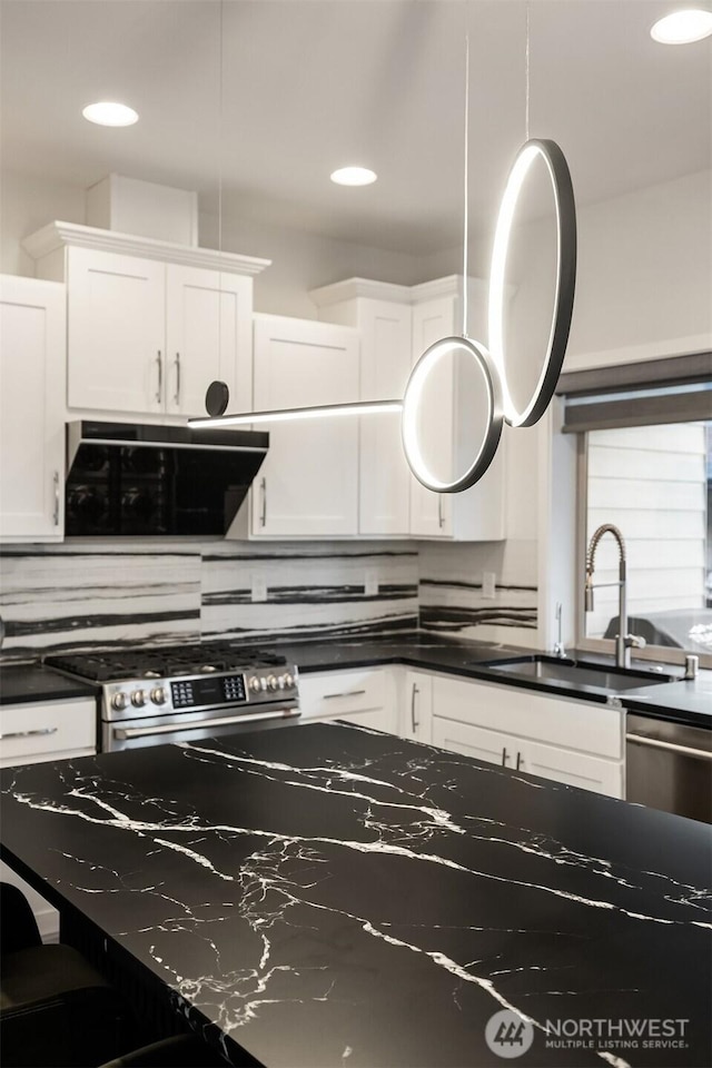 kitchen with dark countertops, white cabinets, stainless steel gas stove, and a sink