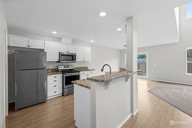 kitchen featuring stainless steel appliances, white cabinetry, a breakfast bar area, and dark stone countertops