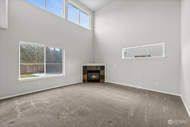 unfurnished living room featuring carpet flooring, a tiled fireplace, and high vaulted ceiling