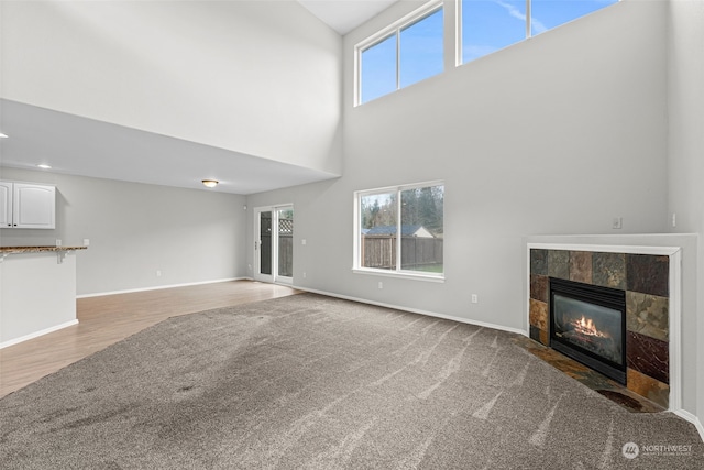 unfurnished living room with a tiled fireplace, a wealth of natural light, light colored carpet, and a high ceiling