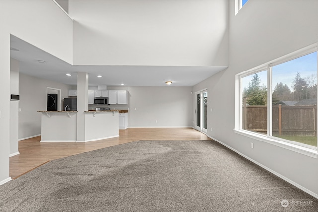 unfurnished living room featuring a towering ceiling and light wood-type flooring