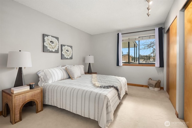 bedroom with rail lighting, light carpet, a textured ceiling, and baseboards