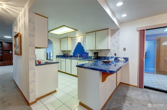 kitchen featuring kitchen peninsula, sink, light carpet, and white cabinets