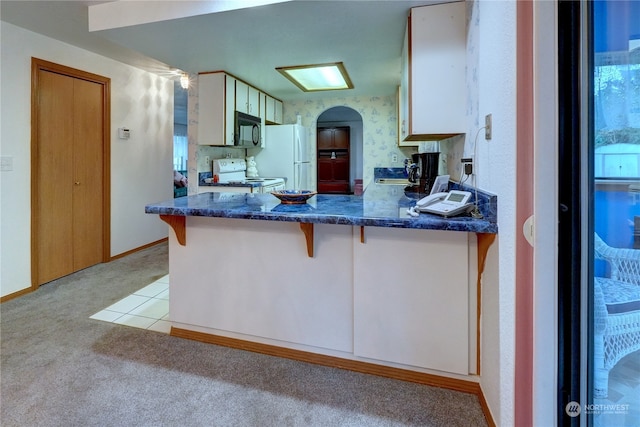 kitchen featuring white appliances, a breakfast bar, white cabinetry, light carpet, and kitchen peninsula