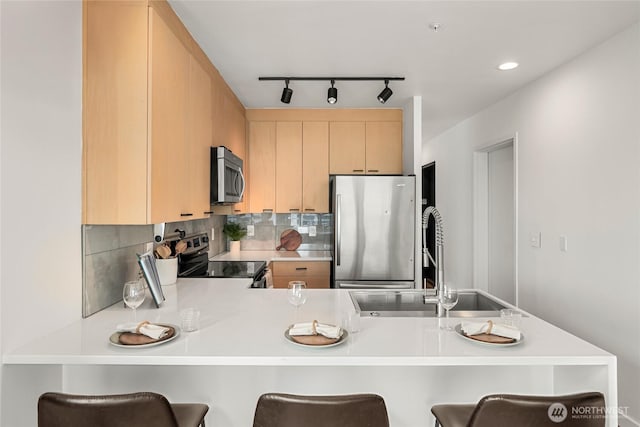 kitchen featuring a breakfast bar, light brown cabinetry, appliances with stainless steel finishes, a sink, and a peninsula