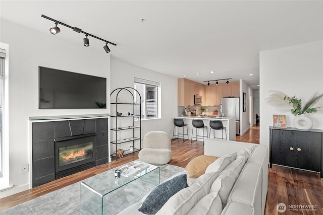 living area featuring a tile fireplace, rail lighting, recessed lighting, and wood finished floors