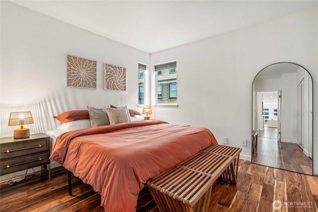 bedroom featuring baseboards, arched walkways, and wood finished floors