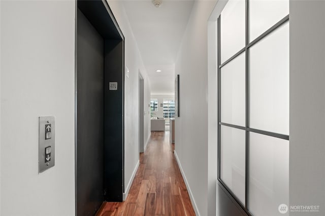 hallway featuring baseboards, wood finished floors, and elevator