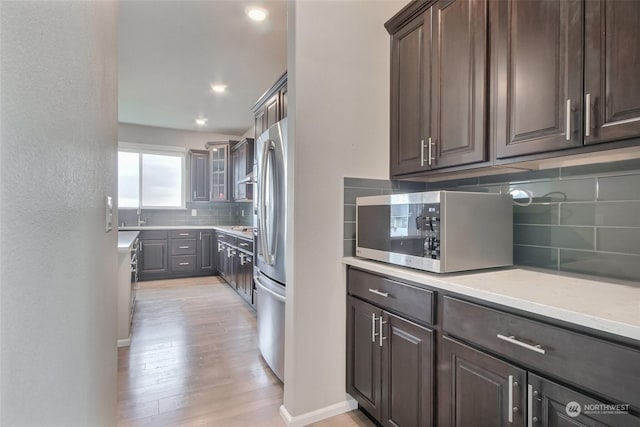 kitchen with stainless steel appliances, dark brown cabinets, backsplash, and light hardwood / wood-style floors