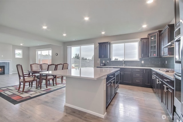 kitchen featuring sink, light hardwood / wood-style flooring, a tile fireplace, backsplash, and a center island