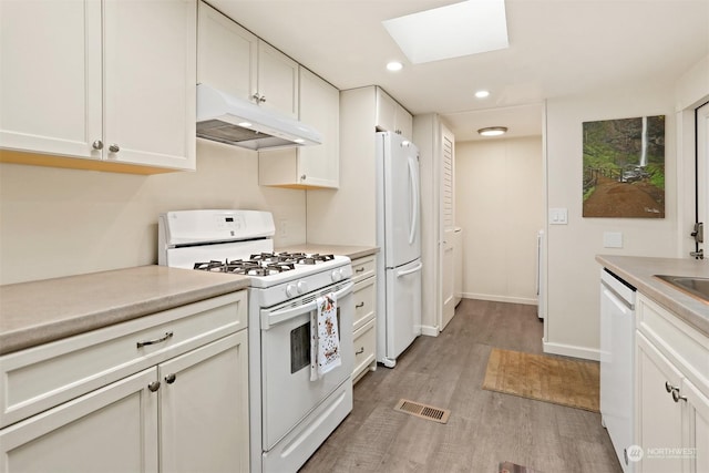 kitchen featuring white appliances, a skylight, light wood-type flooring, and white cabinets