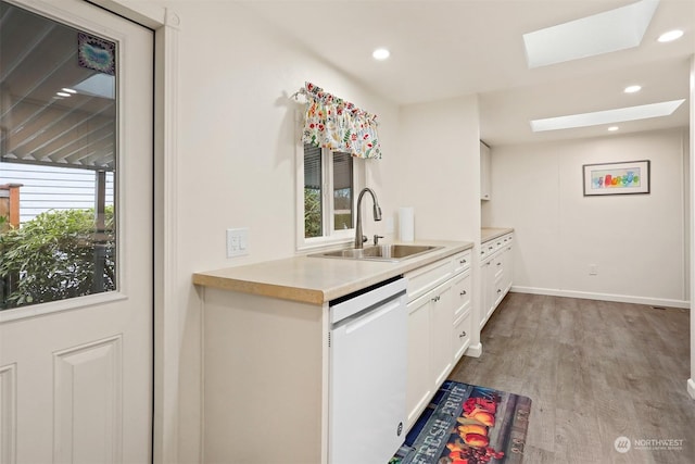 kitchen featuring a skylight, sink, white cabinets, white dishwasher, and light hardwood / wood-style flooring