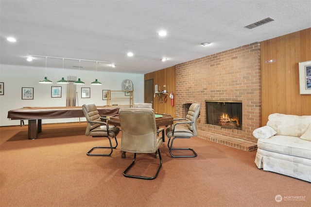 dining room with pool table, a textured ceiling, wooden walls, carpet floors, and a fireplace