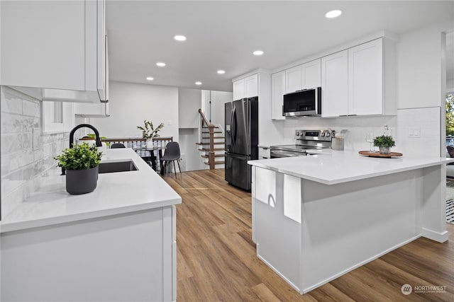 kitchen featuring sink, appliances with stainless steel finishes, white cabinetry, kitchen peninsula, and light wood-type flooring