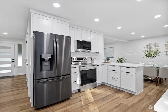 kitchen with stainless steel appliances, white cabinets, light hardwood / wood-style floors, and kitchen peninsula