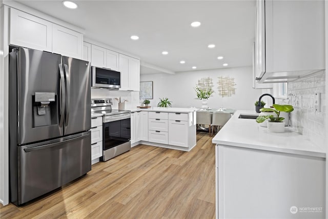 kitchen featuring appliances with stainless steel finishes, sink, white cabinets, decorative backsplash, and light hardwood / wood-style flooring