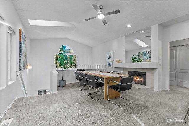 interior space with light carpet, ceiling fan, a fireplace, and vaulted ceiling with skylight