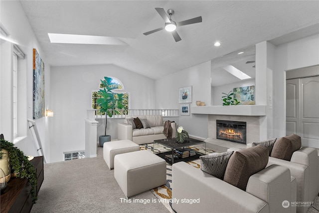 carpeted living room with a tile fireplace, vaulted ceiling with skylight, and ceiling fan