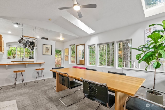 dining space with lofted ceiling with skylight, plenty of natural light, light colored carpet, and ceiling fan