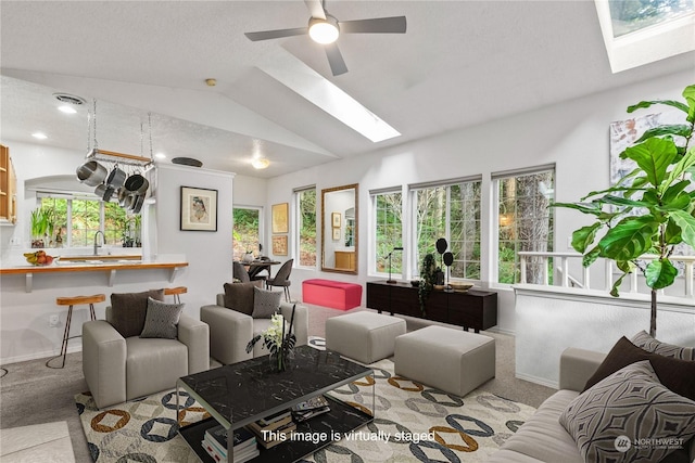 living room with ceiling fan, vaulted ceiling with skylight, and light carpet