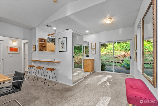 interior space featuring vaulted ceiling, light carpet, a kitchen breakfast bar, and kitchen peninsula