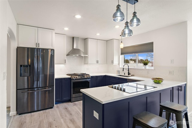 kitchen featuring wall chimney exhaust hood, sink, white cabinetry, pendant lighting, and stainless steel appliances