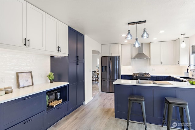 kitchen featuring white cabinetry, sink, stainless steel gas range oven, wall chimney range hood, and fridge with ice dispenser