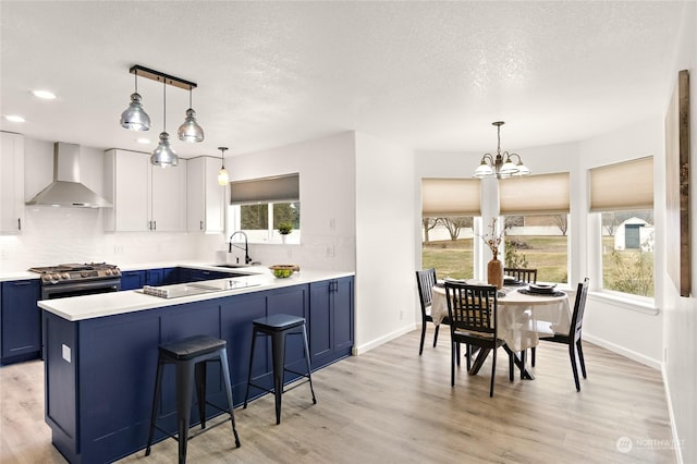 kitchen featuring pendant lighting, white cabinetry, sink, blue cabinetry, and wall chimney exhaust hood