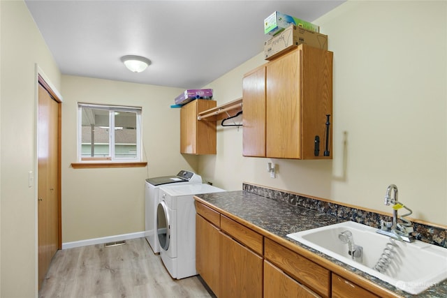 clothes washing area with sink, light hardwood / wood-style floors, cabinets, and washing machine and dryer