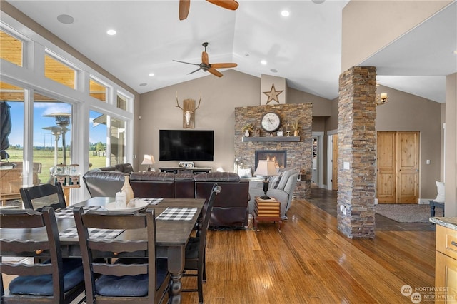 dining space featuring a stone fireplace, high vaulted ceiling, hardwood / wood-style floors, ceiling fan, and decorative columns