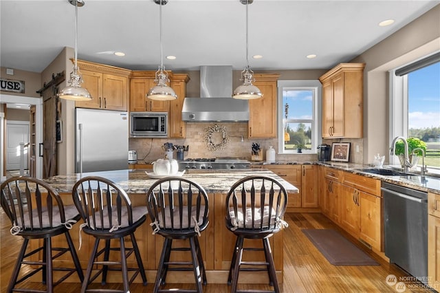 kitchen featuring light stone counters, built in appliances, decorative light fixtures, a kitchen island, and wall chimney range hood