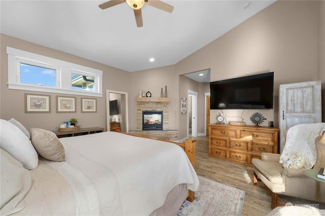 bedroom featuring a stone fireplace, vaulted ceiling, light hardwood / wood-style floors, and ceiling fan