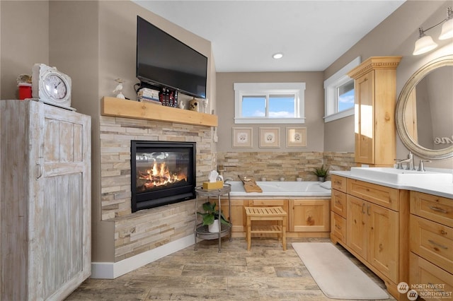 bathroom with vanity, a stone fireplace, and a bathtub