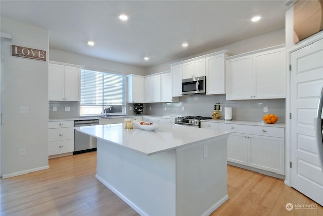 kitchen with stainless steel appliances, a kitchen island, white cabinets, and light hardwood / wood-style floors