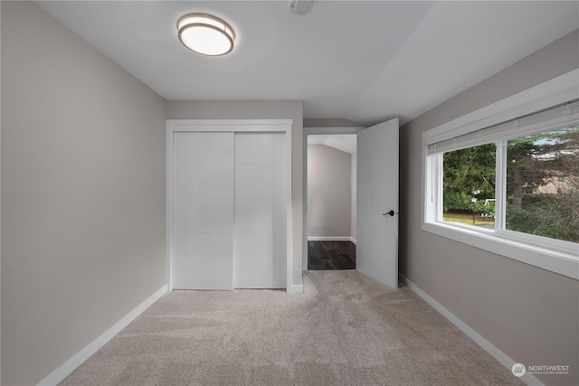 unfurnished bedroom featuring vaulted ceiling, carpet floors, and a closet